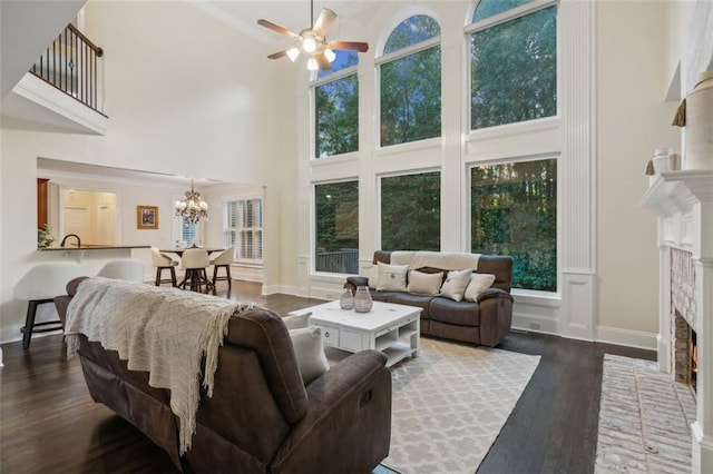 living room with ceiling fan with notable chandelier, dark hardwood / wood-style floors, a high ceiling, and a brick fireplace