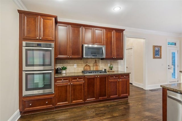 kitchen featuring tasteful backsplash, dark stone counters, dark wood-type flooring, stainless steel appliances, and crown molding