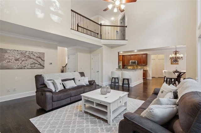 living area with ceiling fan with notable chandelier, a high ceiling, dark wood-style flooring, baseboards, and ornamental molding