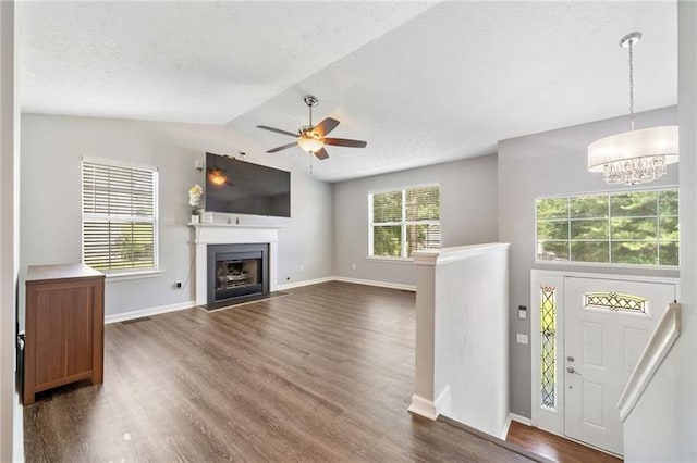 unfurnished living room with ceiling fan with notable chandelier, dark wood-type flooring, a textured ceiling, and vaulted ceiling