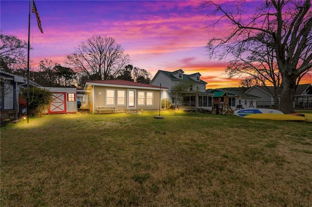 back house at dusk with a lawn and a storage unit