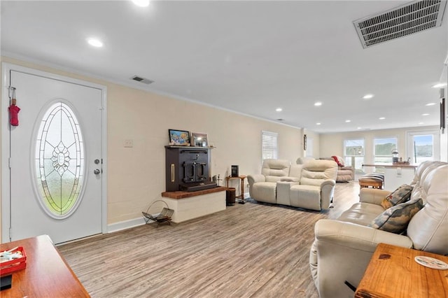 living room with a wood stove, light hardwood / wood-style flooring, and ornamental molding