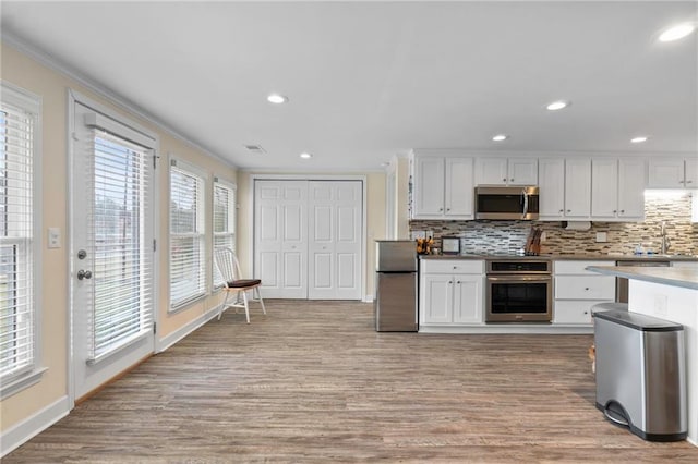 kitchen featuring sink, light wood-type flooring, appliances with stainless steel finishes, tasteful backsplash, and white cabinetry