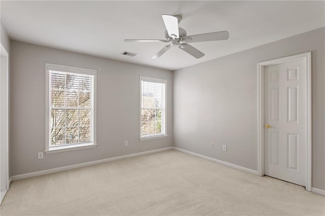 spare room featuring a ceiling fan, light colored carpet, visible vents, and baseboards