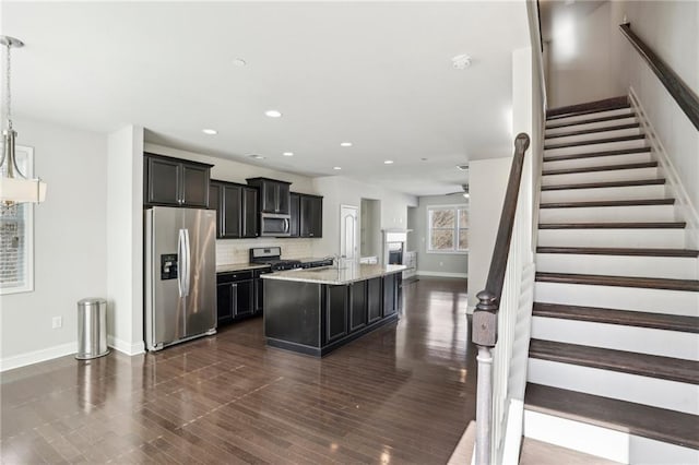 kitchen with tasteful backsplash, decorative light fixtures, stainless steel appliances, light stone countertops, and a kitchen island with sink