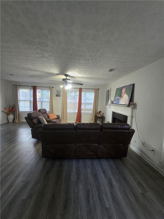 living room featuring dark wood-type flooring, a wealth of natural light, ceiling fan, and a textured ceiling