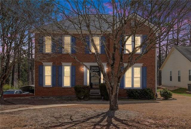 colonial home featuring central air condition unit and brick siding