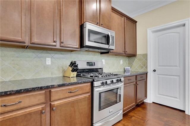 kitchen featuring dark wood-type flooring, dark stone countertops, ornamental molding, tasteful backsplash, and stainless steel appliances