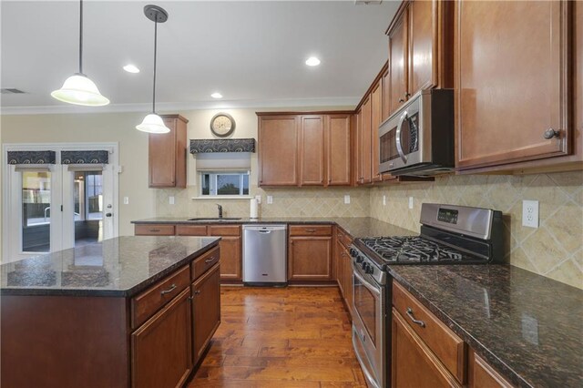 kitchen featuring hanging light fixtures, dark hardwood / wood-style flooring, dark stone countertops, appliances with stainless steel finishes, and ornamental molding