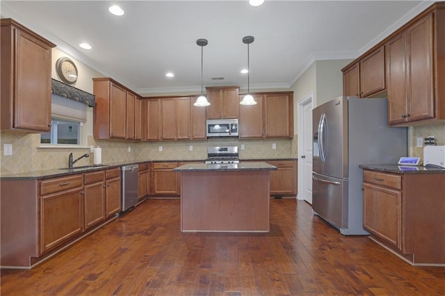 kitchen with hanging light fixtures, sink, ornamental molding, appliances with stainless steel finishes, and a kitchen island