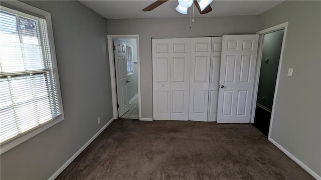 unfurnished bedroom with dark colored carpet, a closet, and ceiling fan