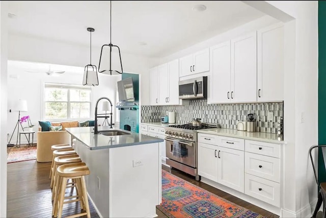 kitchen with sink, hanging light fixtures, white cabinetry, stainless steel appliances, and a center island with sink