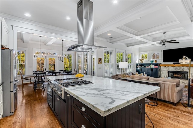 kitchen with appliances with stainless steel finishes, ceiling fan with notable chandelier, island range hood, a kitchen bar, and coffered ceiling