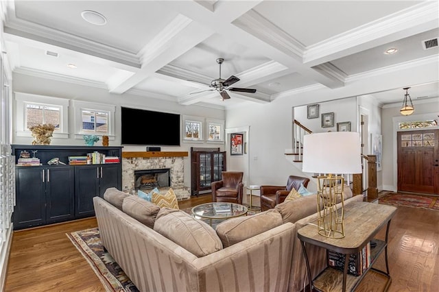living room with a ceiling fan, wood finished floors, beam ceiling, stairway, and a fireplace with raised hearth