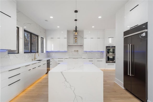 kitchen with white cabinetry, built in refrigerator, a center island, hanging light fixtures, and light stone countertops