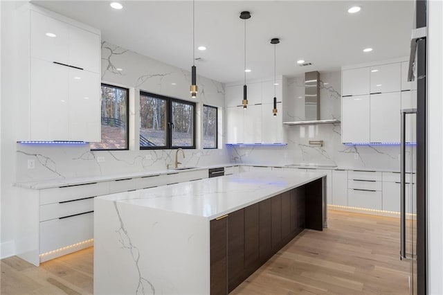 kitchen featuring wall chimney range hood, sink, hanging light fixtures, a center island, and white cabinets