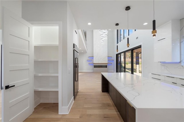 kitchen with dark brown cabinets, light stone counters, white cabinets, decorative light fixtures, and light wood-type flooring