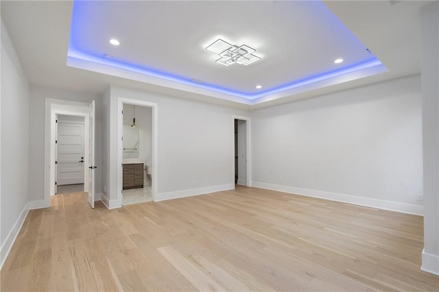 unfurnished bedroom with connected bathroom, a tray ceiling, and light wood-type flooring