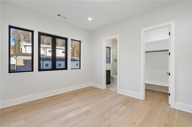 unfurnished bedroom featuring a spacious closet, light hardwood / wood-style flooring, a closet, and ensuite bathroom