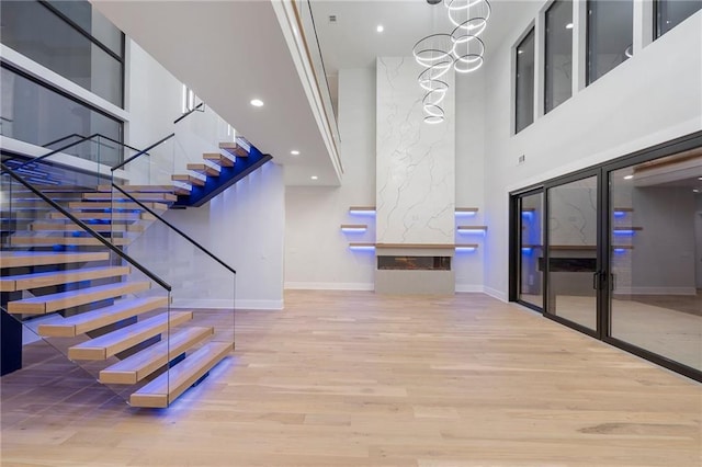 staircase with a towering ceiling, wood-type flooring, and a chandelier