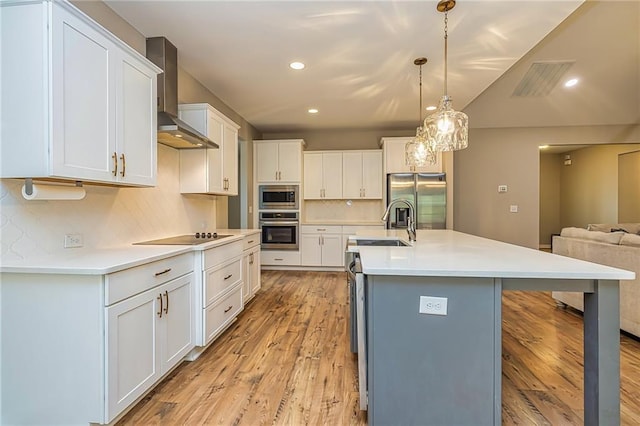 kitchen with decorative backsplash, appliances with stainless steel finishes, wall chimney range hood, decorative light fixtures, and white cabinetry