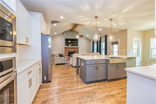 kitchen with white cabinetry, stainless steel appliances, a fireplace, gray cabinets, and a center island with sink