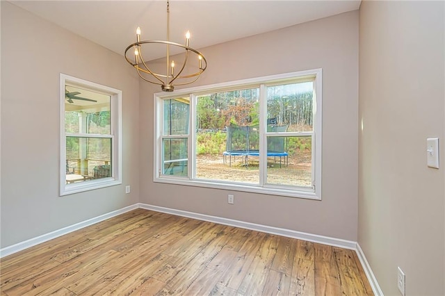 unfurnished dining area with ceiling fan with notable chandelier, light hardwood / wood-style flooring, and plenty of natural light