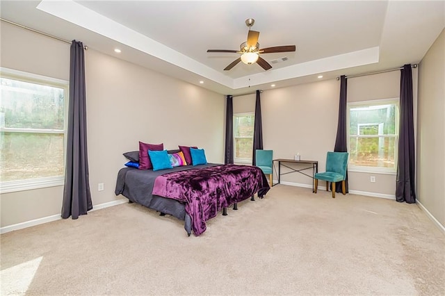 carpeted bedroom featuring multiple windows, a raised ceiling, and ceiling fan