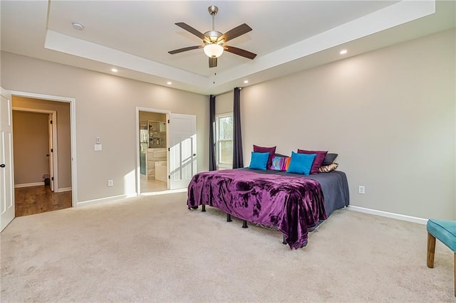 carpeted bedroom with a tray ceiling, ensuite bath, and ceiling fan