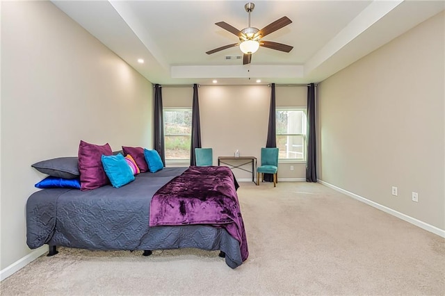 bedroom featuring a tray ceiling, multiple windows, ceiling fan, and carpet