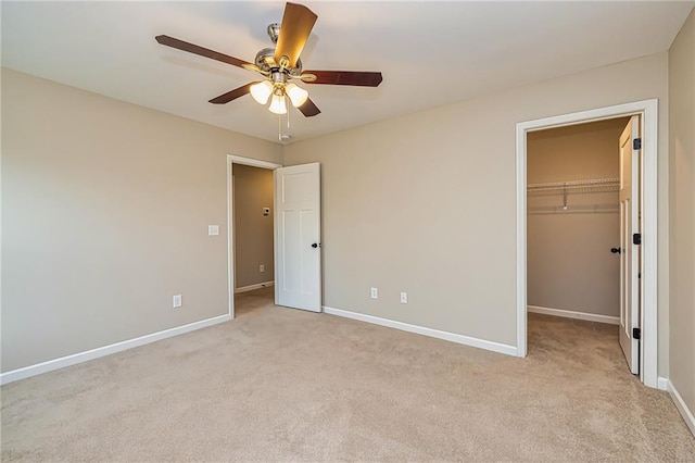 unfurnished bedroom with light carpet, a walk in closet, a closet, and ceiling fan