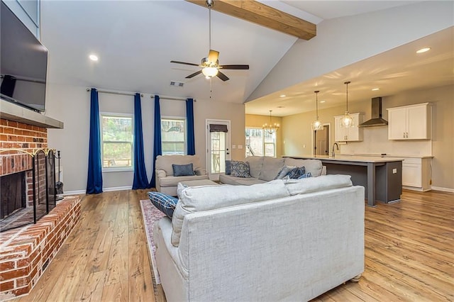 living room with ceiling fan with notable chandelier, lofted ceiling with beams, sink, light hardwood / wood-style flooring, and a fireplace