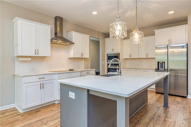 kitchen with a center island with sink, wall chimney exhaust hood, light hardwood / wood-style floors, white cabinetry, and stainless steel appliances