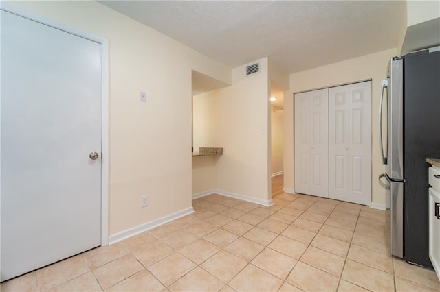 unfurnished bedroom featuring freestanding refrigerator, light tile patterned floors, a closet, and baseboards