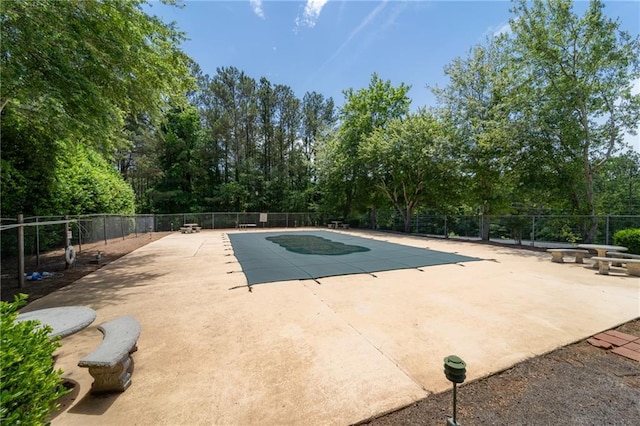 view of swimming pool featuring fence, a patio, and view of wooded area