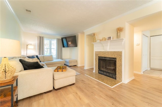 living room featuring ornamental molding, a fireplace with raised hearth, light wood-style flooring, a textured ceiling, and baseboards