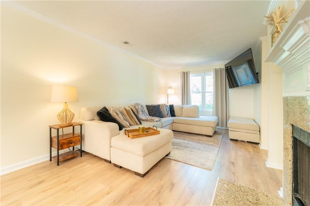living room featuring a fireplace, light wood finished floors, baseboards, and crown molding