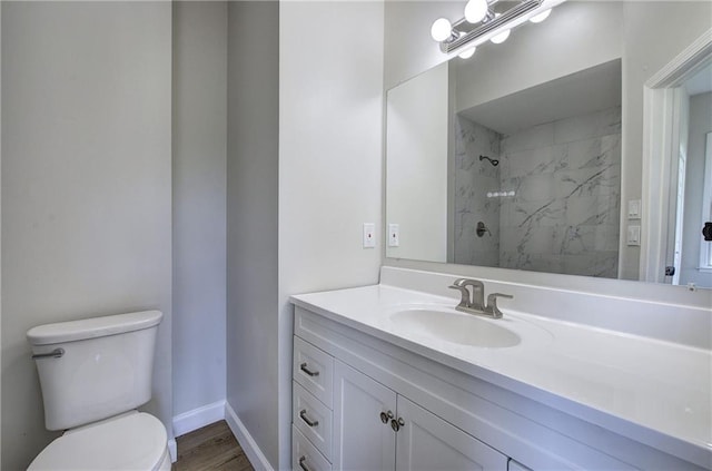 bathroom with toilet, a tile shower, vanity, wood finished floors, and baseboards