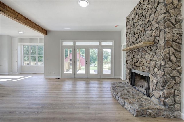unfurnished living room featuring baseboards, wood finished floors, a stone fireplace, beam ceiling, and french doors