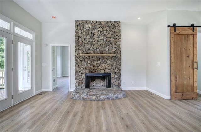 unfurnished living room with wood finished floors, baseboards, a fireplace, and a barn door