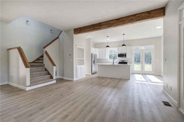 unfurnished living room featuring a sink, light wood-style floors, beam ceiling, baseboards, and stairs