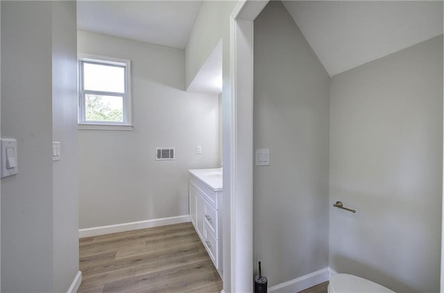 bathroom with wood finished floors, vanity, baseboards, toilet, and lofted ceiling