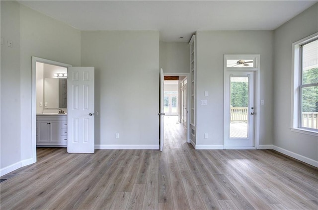 unfurnished bedroom with light wood finished floors, baseboards, and ensuite bathroom