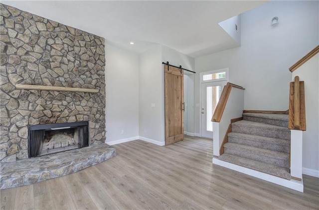 unfurnished living room featuring a barn door, baseboards, stairs, and wood finished floors