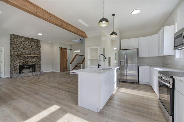 kitchen featuring stainless steel appliances, a barn door, a sink, light wood-style floors, and white cabinetry