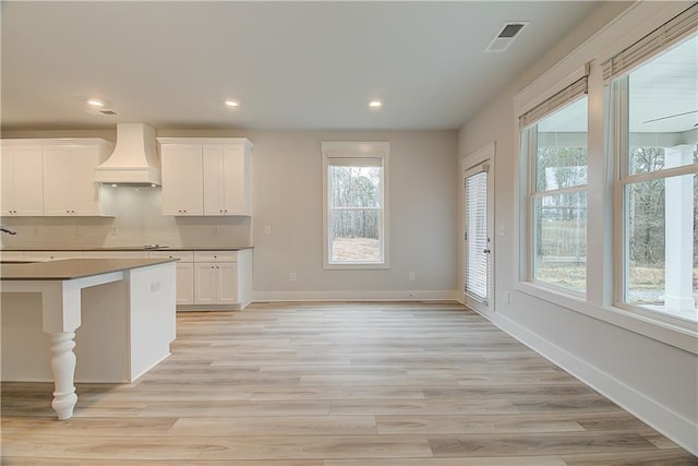 kitchen with premium range hood, plenty of natural light, white cabinets, and light hardwood / wood-style flooring