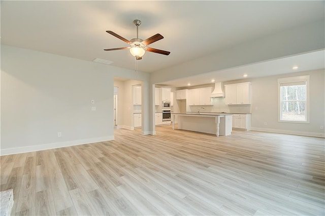 unfurnished living room featuring ceiling fan, light hardwood / wood-style floors, and sink