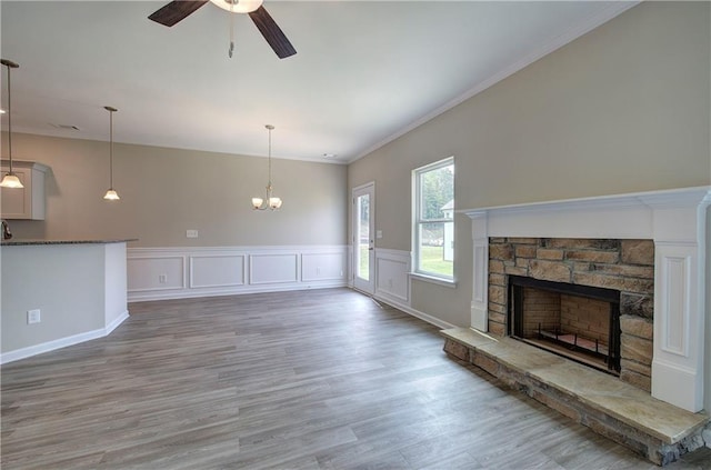 unfurnished living room featuring hardwood / wood-style flooring, ornamental molding, a stone fireplace, and ceiling fan with notable chandelier