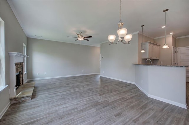 unfurnished living room with a stone fireplace, wood-type flooring, sink, ornamental molding, and ceiling fan