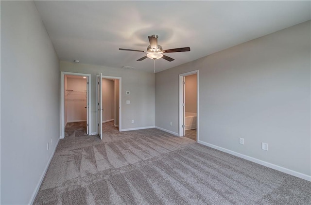 unfurnished bedroom featuring ceiling fan, connected bathroom, light carpet, a walk in closet, and a closet